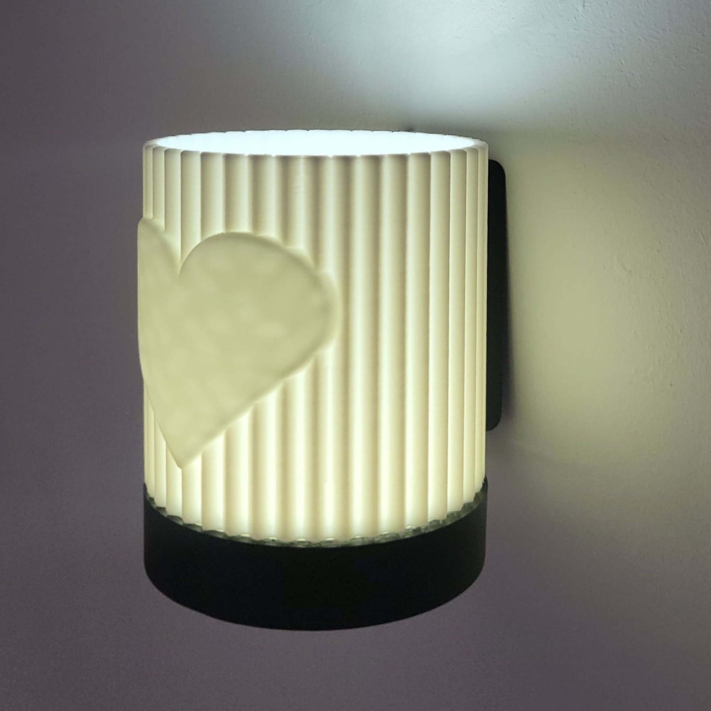 Wall-mounted light fixture with ribbed design and heart cutout on a dark background