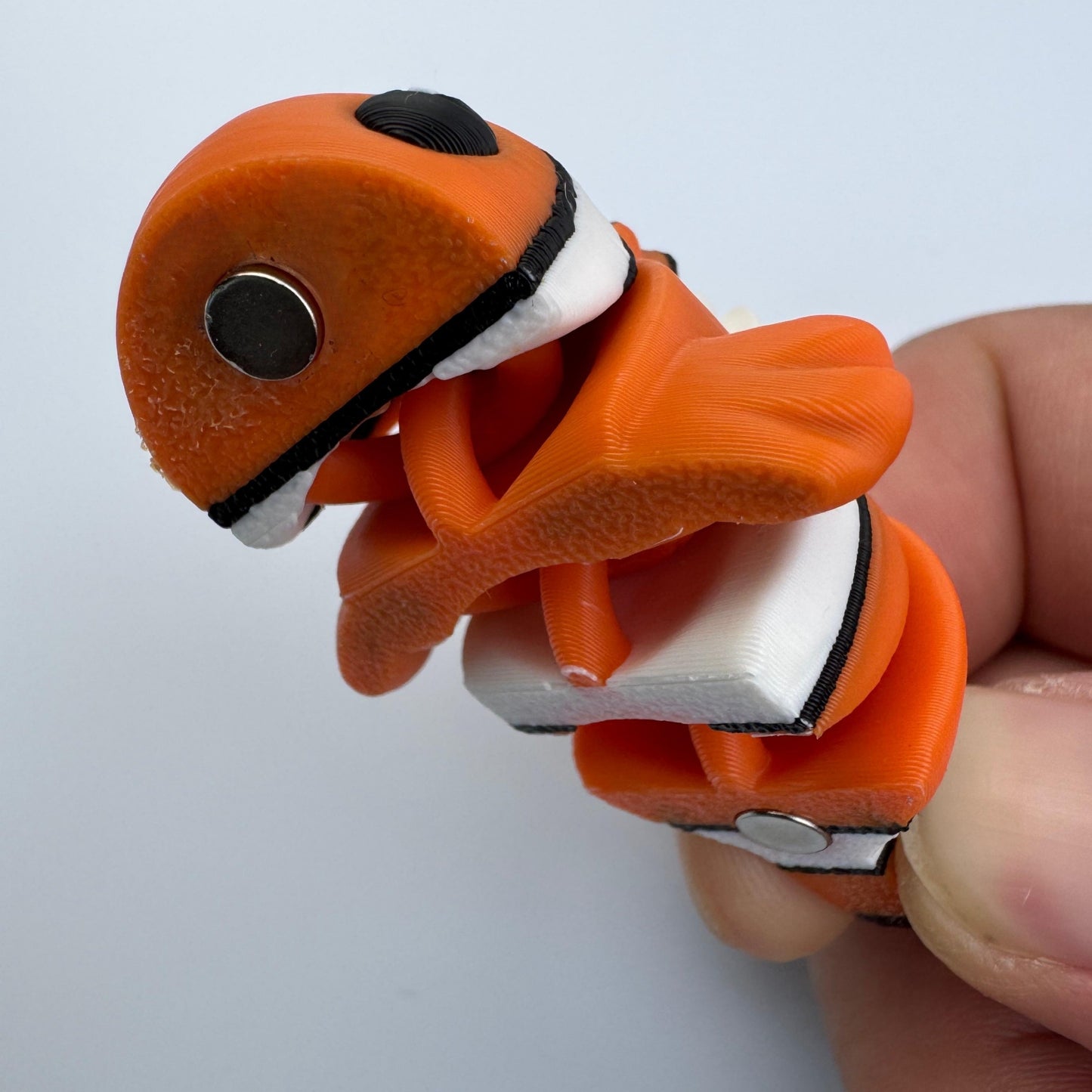 Orange and white tool with a black button held by a hand on a light gray background