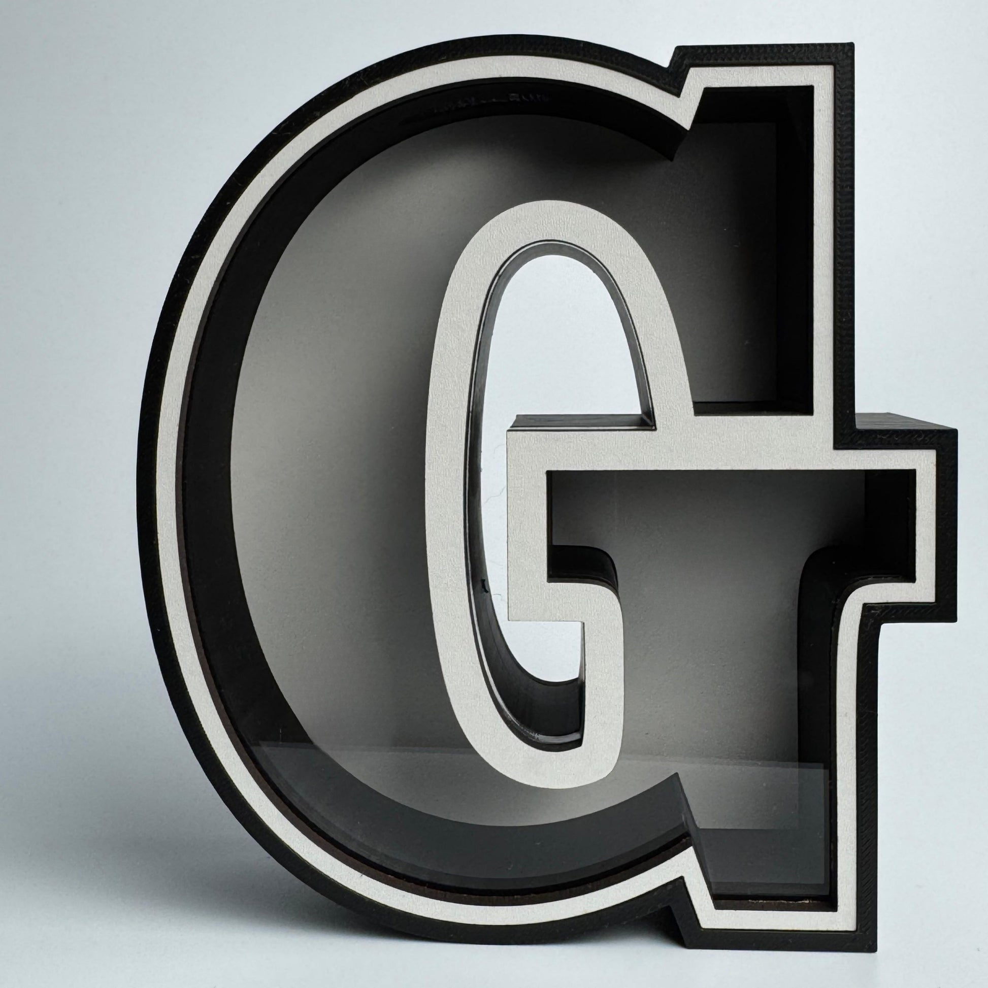3D letter 'G' with a metallic finish on a light gray background