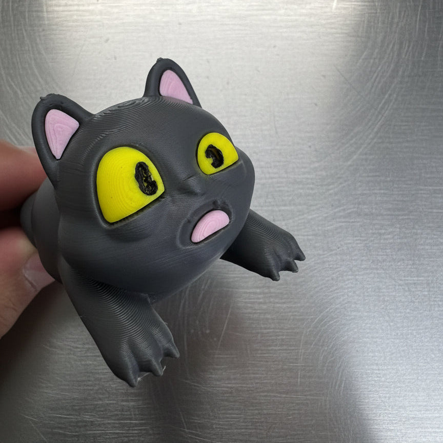 Black cat-shaped toy with yellow eyes and pink ears on a metallic surface