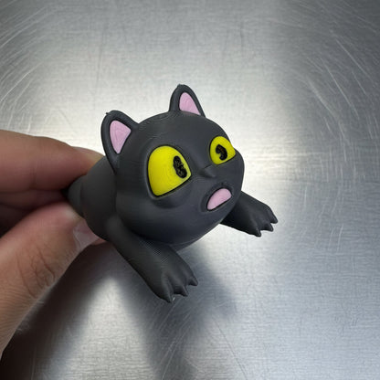 Black cat figurine with yellow eyes and pink ears held by a hand on a metallic surface