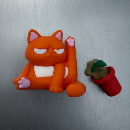 Orange cat-shaped object with a small potted plant on a metallic surface