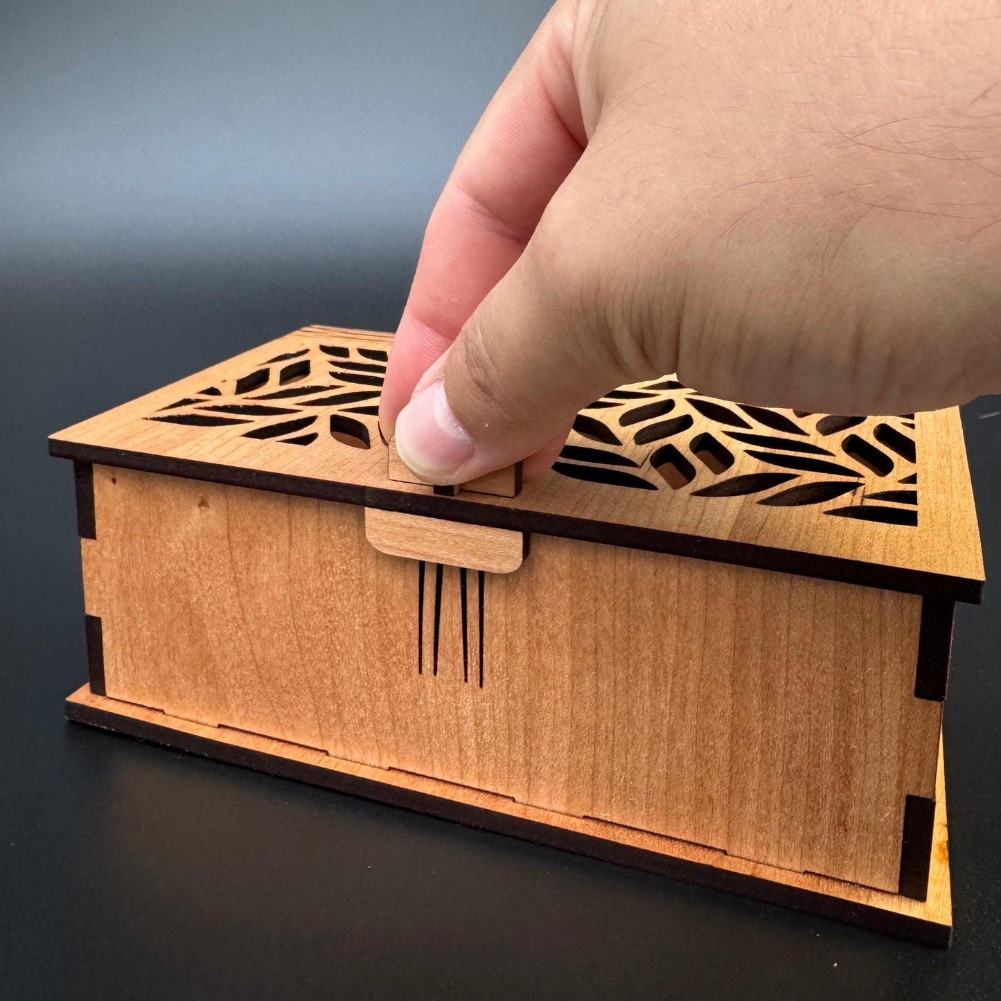 Wooden box with laser-cut design held by a hand against a dark background