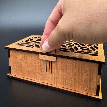 Wooden box with laser-cut design held by a hand against a dark background
