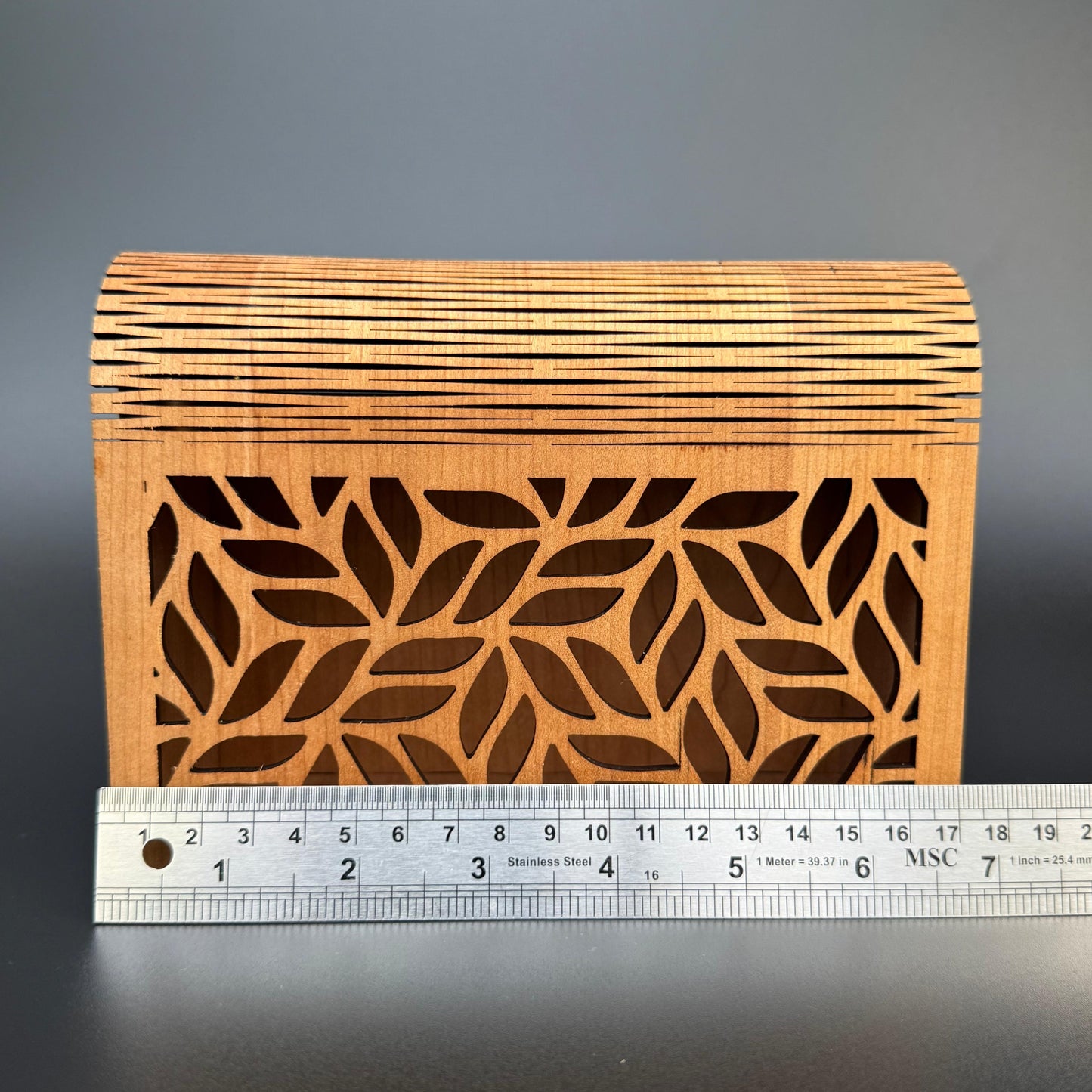 Wooden box with leaf pattern and a ruler for scale on a dark background