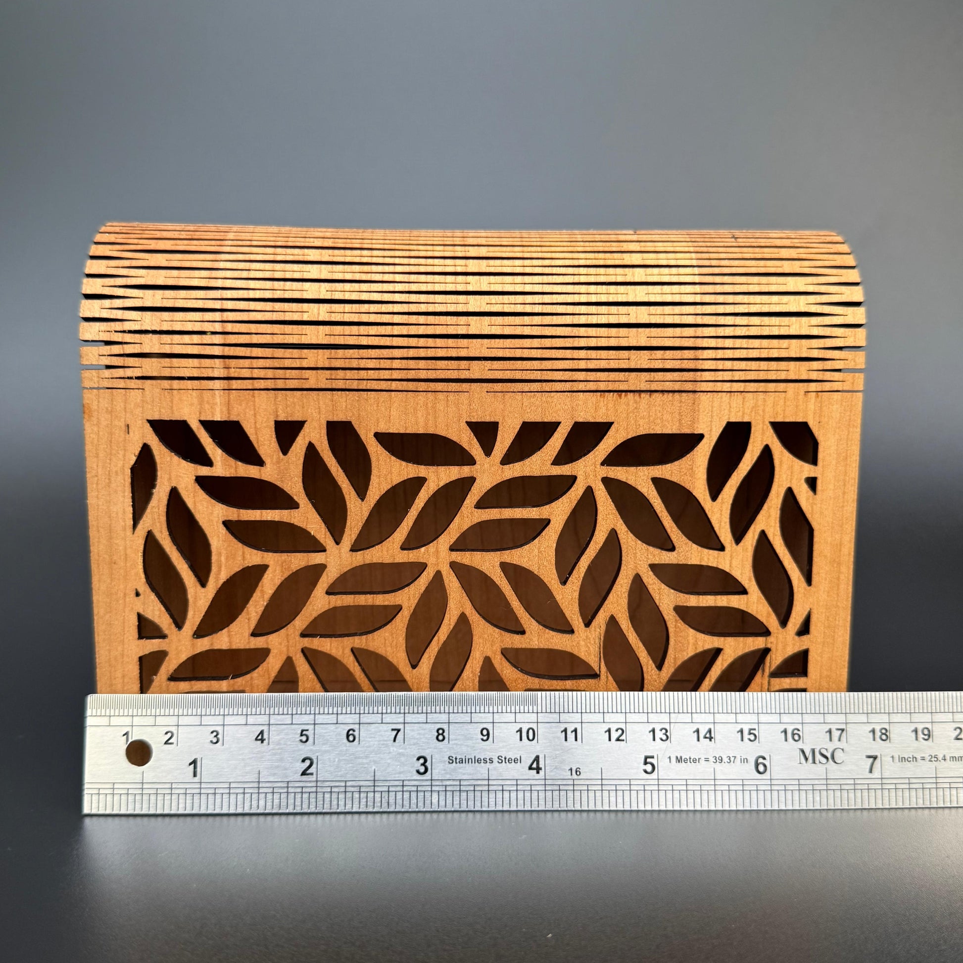 Wooden box with leaf pattern and a ruler for scale on a dark background