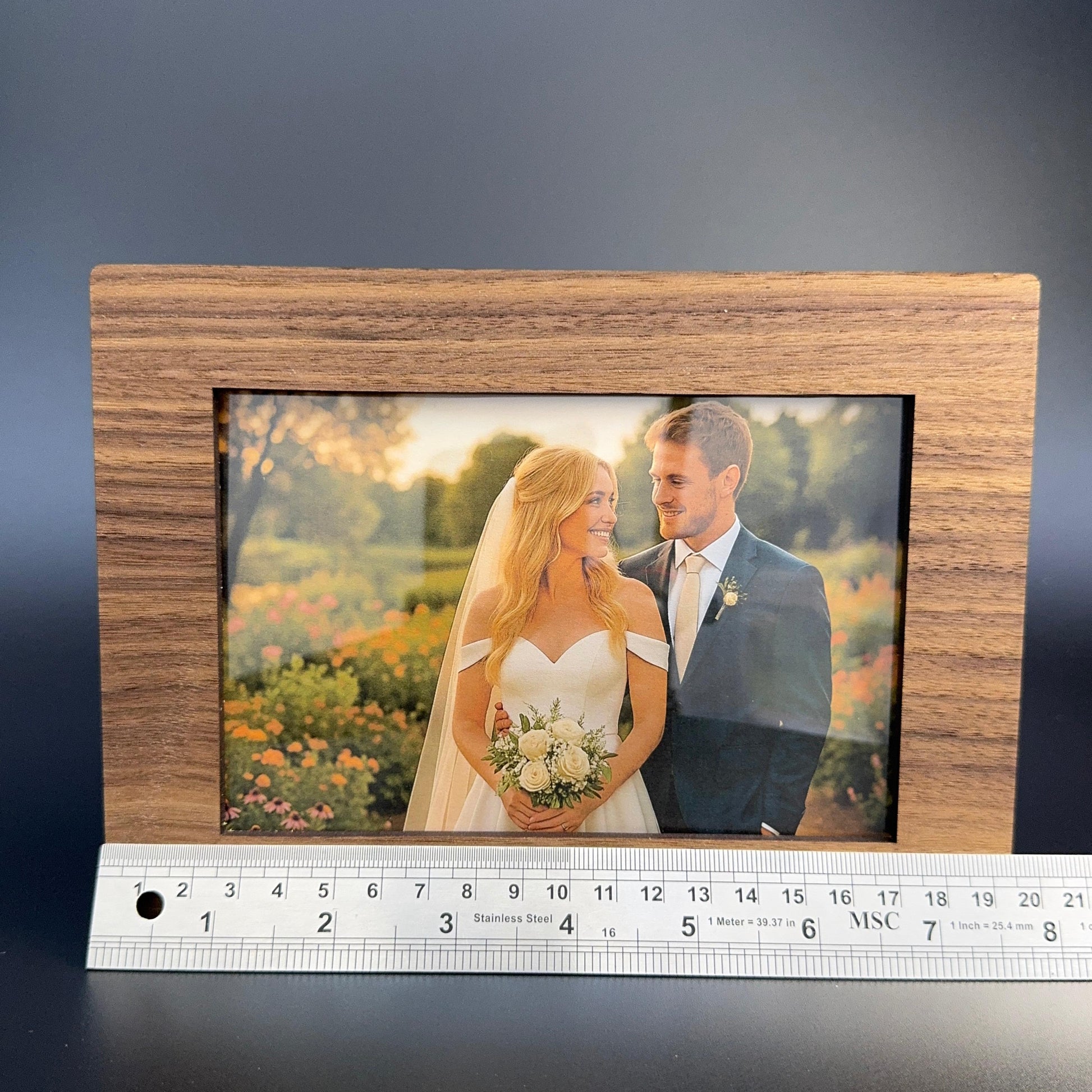 Wooden photo frame with a couple's picture and a ruler for scale on a dark background