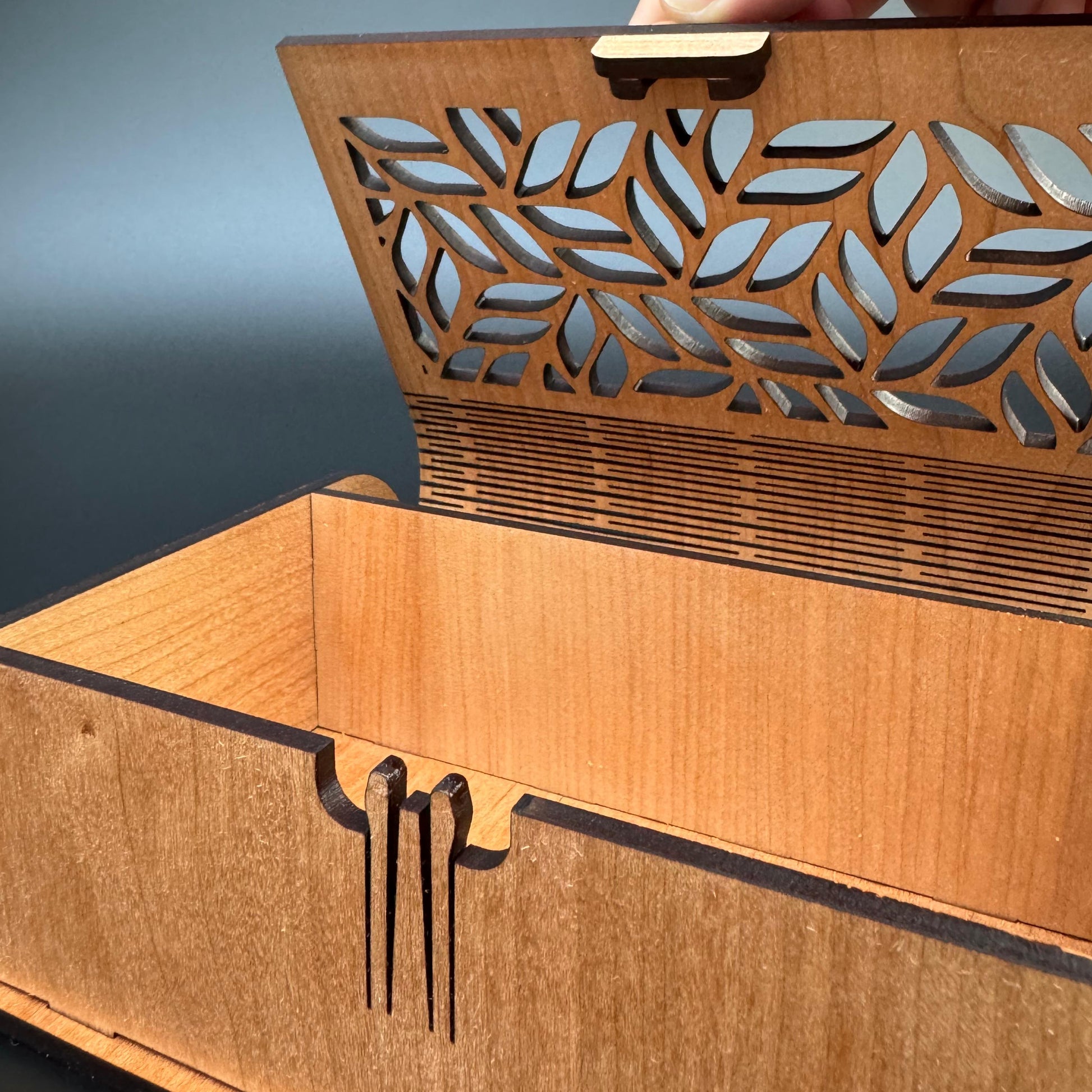 Wooden box with laser-cut leaf design on a gray background
