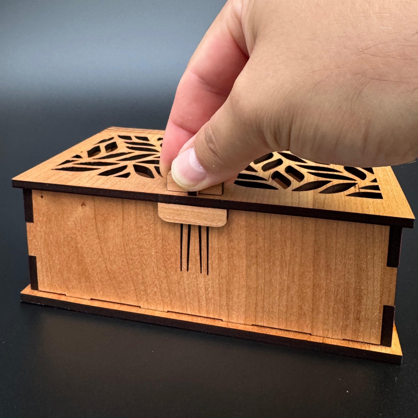 Wooden box with laser cut design held by a hand against a dark background