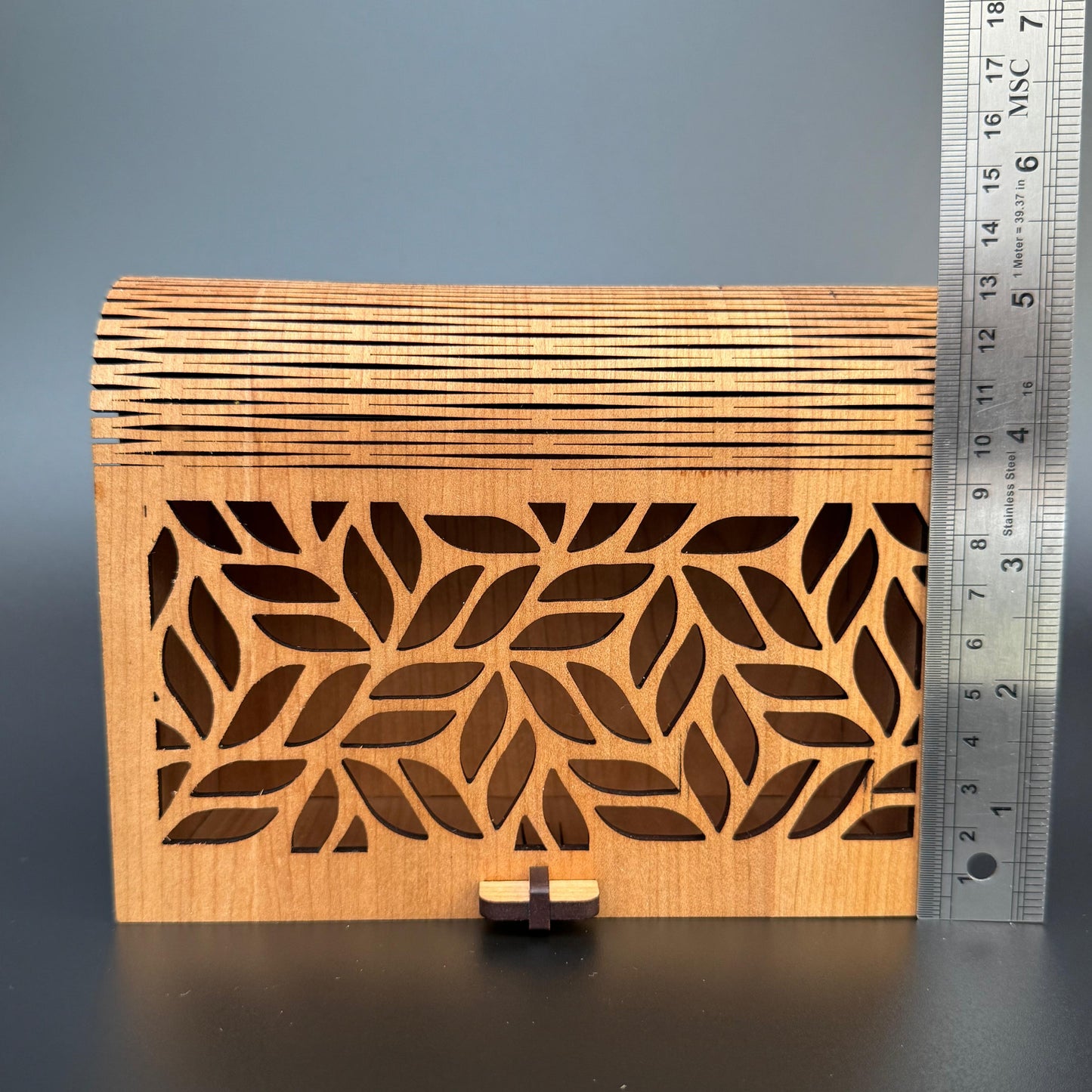 Wooden box with laser-cut leaf pattern next to a ruler on a gray background