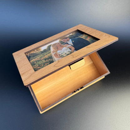 Wooden box with a glass lid displaying a couple in an embrace, set against a gradient blue background.