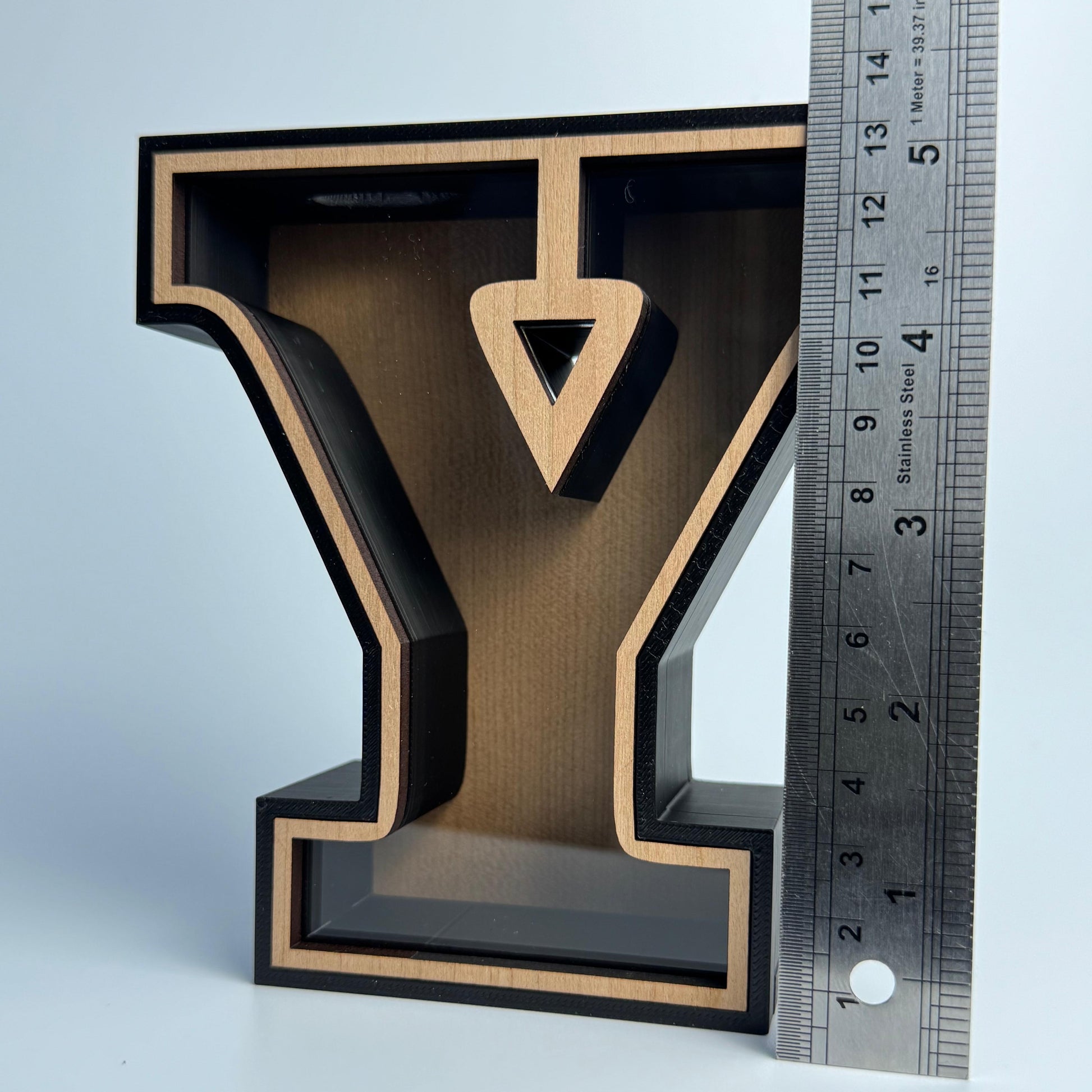 Wooden letter 'Y' with black border and arrow cutout, next to a ruler for scale on a light blue background.