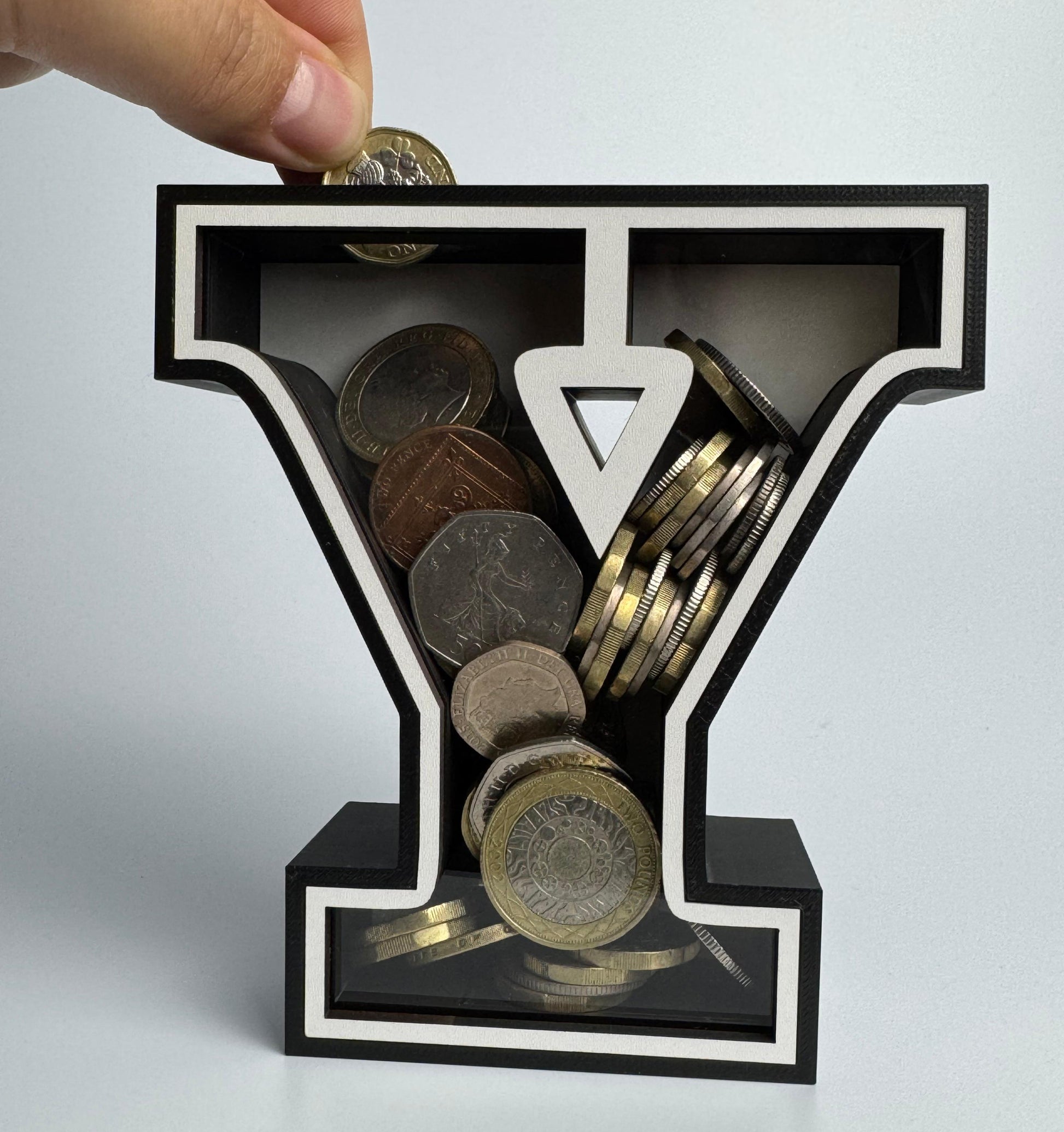 Hand placing coins into a black letter 'Y' shaped container on a light gray background