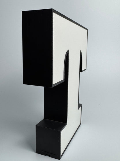 Black and white letter 'T' sculpture on a gray background