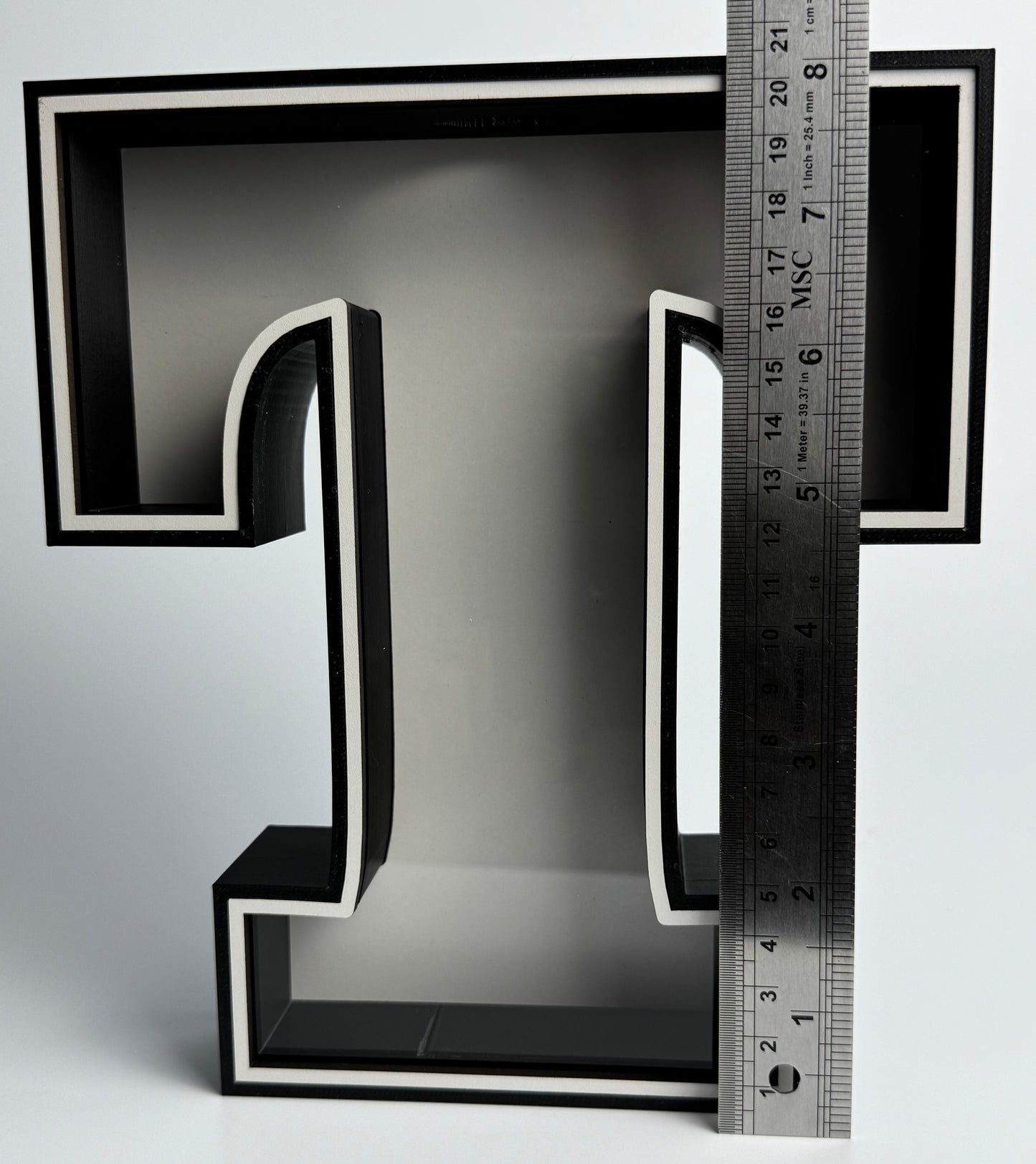Black letter 'L' with a ruler for scale on a gray background