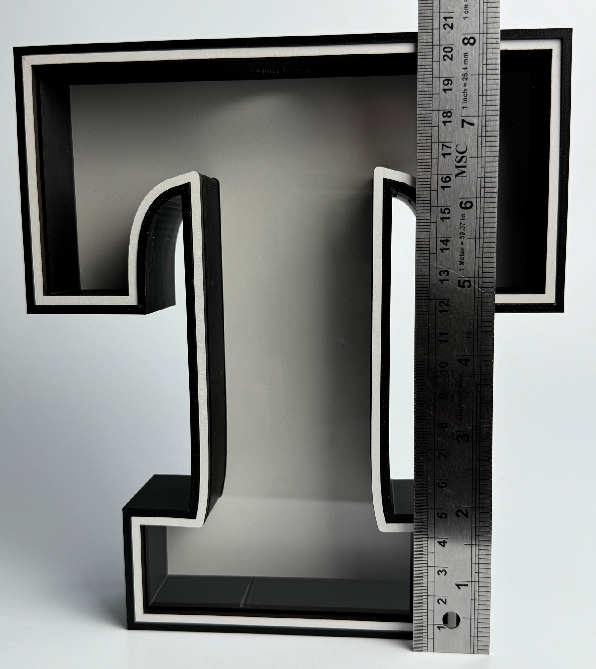 Black letter 'L' with a ruler for scale on a gray background