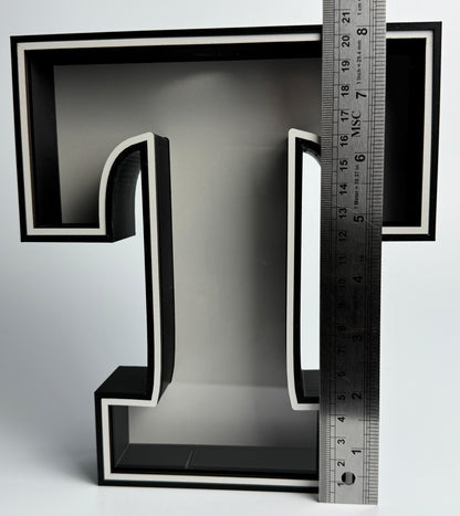 Black letter 'L' with a ruler for scale on a gray background