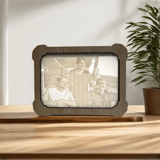 Wooden photo frame with engraved picture of three people on a wooden surface with a plant in the background.