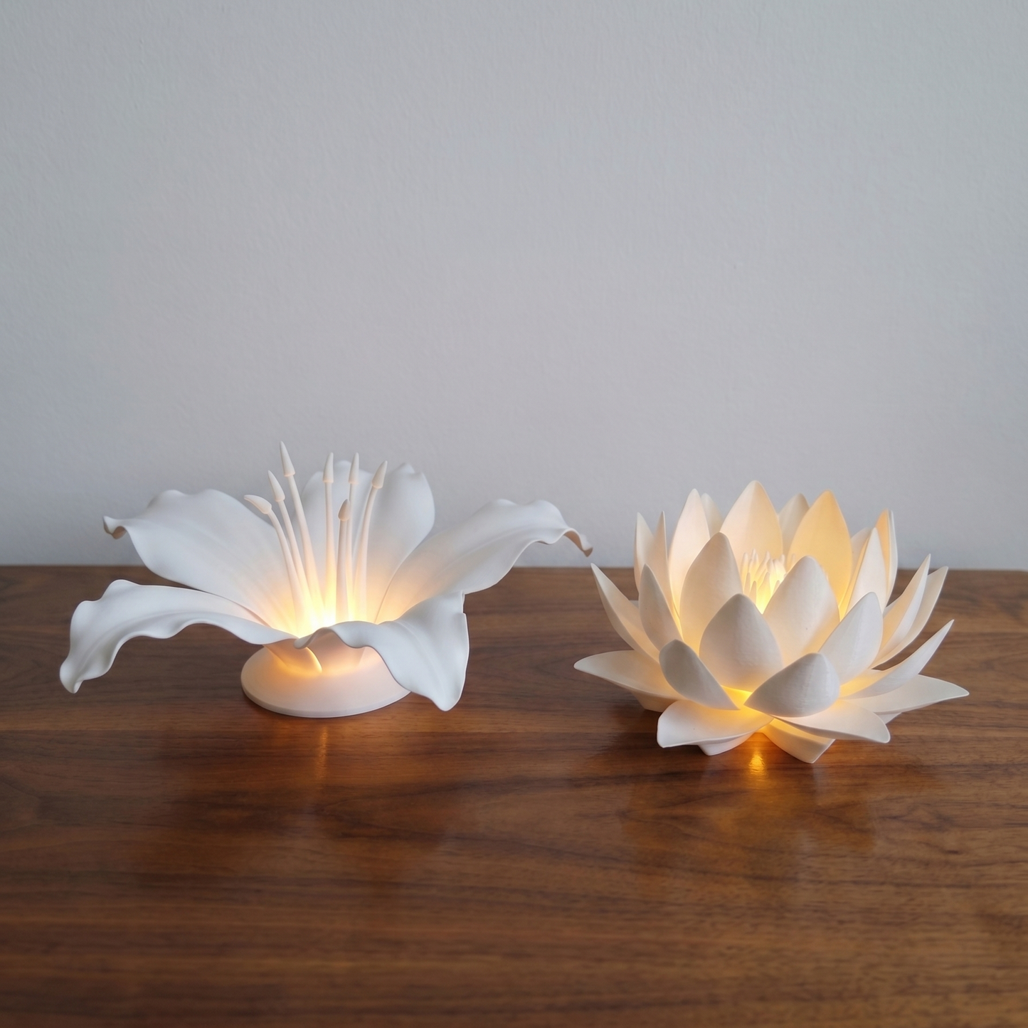 Two white flower-shaped lamps on a wooden surface with a plain background